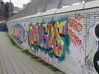848180 Afbeelding van graffiti met verschillende teksten, op een muur langs het voetpad onder de sporen aan de ...